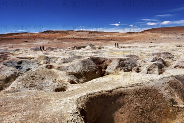 Vast, barren rocky landscape in the desert, two people on the horizon, blue sky, the mud volcanoes and fumaroles on the Altiplano in Bolivia