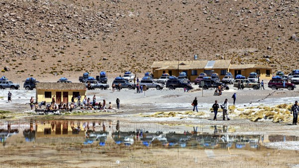 Car park and building in a barren desert landscape with a reflecting lake, The Aguas Termales de Polques in Bolivia