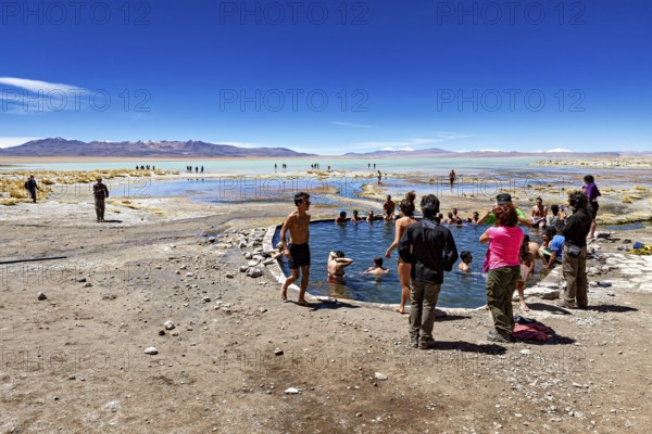 People enjoy a dip in a lake in the middle of a dry, barren desert landscape, The Aguas Termales de Polques in Bolivia