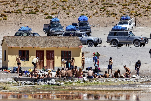 Group of people and cars in front of a small building in a desert landscape, The Aguas Termales de Polques in Bolivia