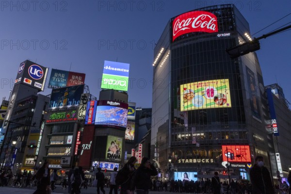 Crowd crossing the zebra crossings of Shibuya Crossing, world-famous intersection in Shibuya district, behind it neon signs and billboards on skyscrapers at dusk, tourist attraction, landmark, Shibuya district, Tokyo, Japan