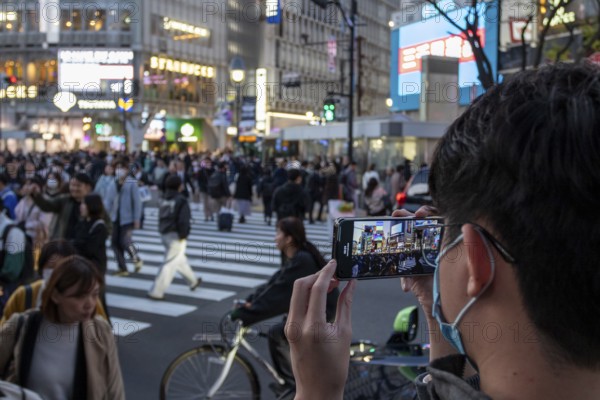 A tourist films the crowd at the zebra crossing of Shibuya Crossing with his smartphone, world-famous crossing in the Shibuya district, tourist attraction, sight, Shibuya district, Tokyo, Japan