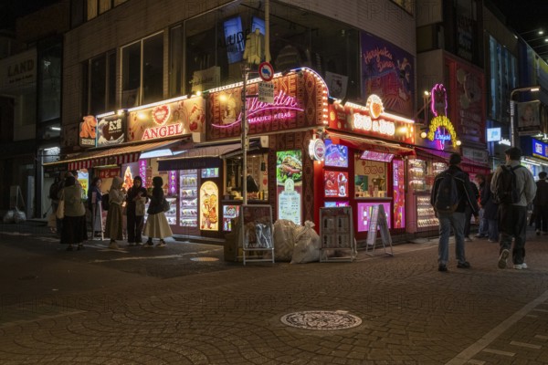 Tourists in front of a shop with illuminated advertisement for kebab and Japanese crepes in Takeshita-dori, Takeshita Street, alley with souvenir shops and restaurants in Harajuku neighbourhood at night, tourist attraction, sight, Shibuya district, Tokyo, Japan