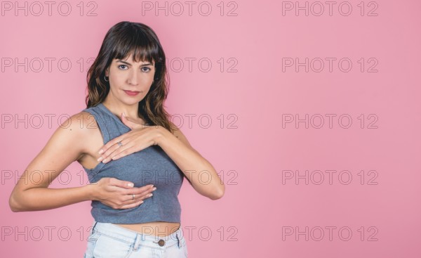 Young woman performing self-breast exam against pink background with copy space