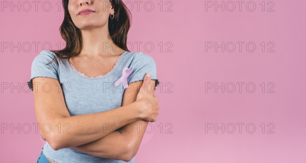 Young woman embracing herself with a pink breast cancer awareness ribbon and copy space