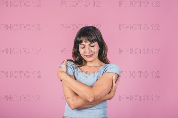 Young woman with eyes closed hugging herself for breast cancer awareness