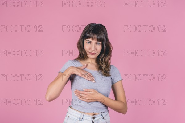 Young woman in gray t-shirt performing breast self-exam on pink background