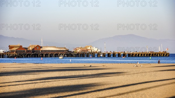A panoramic view of Stearns Wharf and the beach in Santa Barbara, featuring the iconic pier buildings, a sandy shore, and distant mountains