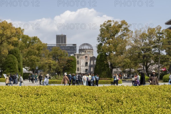 Tourists in the Peace Park with a view of the ruins of the Atomic Bomb Dome, landmark, UNESCO World Heritage Site, peace memorial and memorial to the victims of the atomic bombing of Hiroshima, Naka Ward, Hiroshima, Japan