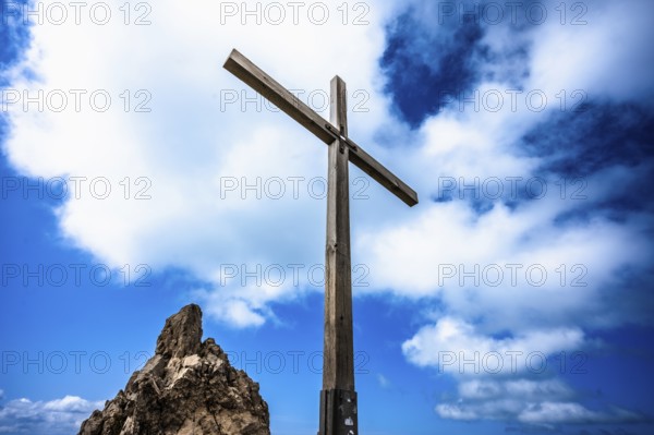 A wooden cross on a rock under a blue sky with white clouds. Kleinwalsertal Vorarlberg Austria Kanzelwand