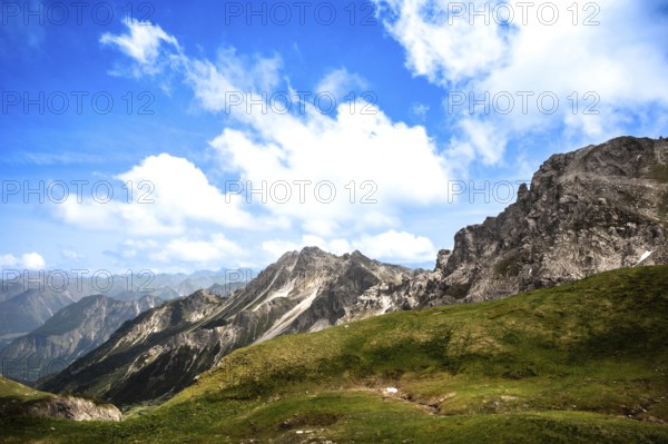Green hills and rocky mountains under a clear blue sky with clouds. Kleinwalsertal Vorarlberg Austria