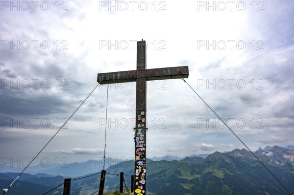 Large wooden cross on a mountain peak with a view of the surrounding Alpine peaks. Kleinwalsertal Vorarlberg Austria