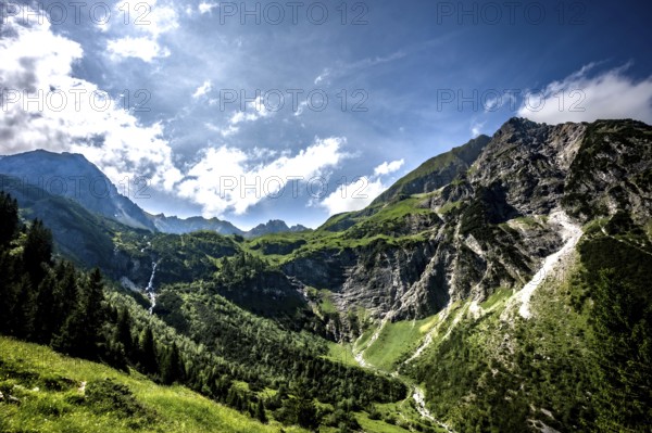 Sunny mountain scene with green slopes and dramatic clouds over the mountains. Kleinwalsertal Vorarlberg Austria