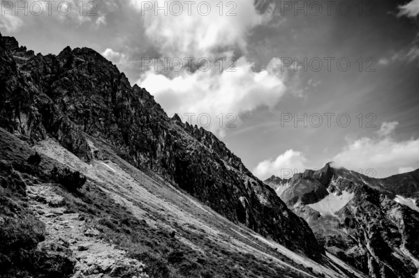 Dramatic black and white view of a rocky mountain landscape under a cloudy sky. Kleinwalsertal Vorarlberg Austria