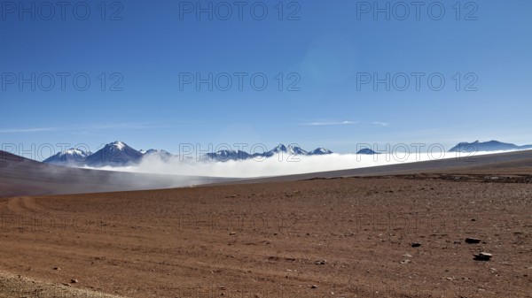 Dry desert plain with distant mountains and wafts of mist under a clear sky, The landscape at San Pedro de Atacama in Chile