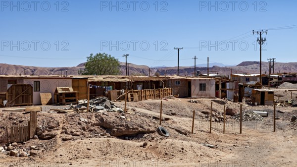 An arid landscape with simple buildings and electricity pylons under a clear sky, The town of San Pedro de Atacama in Chile