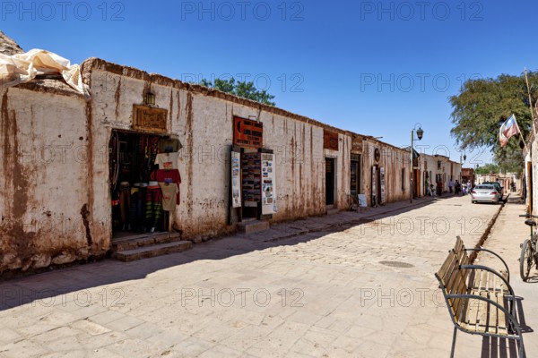 A quiet stretch of street with shops in old buildings along a cobbled path under a blue sky, The town of San Pedro de Atacama in Chile