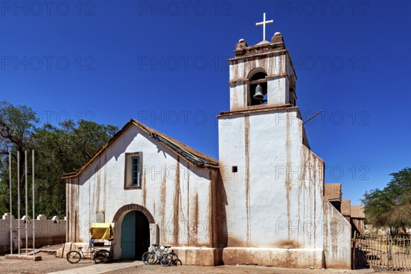 Historic church with bicycle in front of a clear blue sky, cross on the bell tower, The church of San Pedro de Atacama in Chile