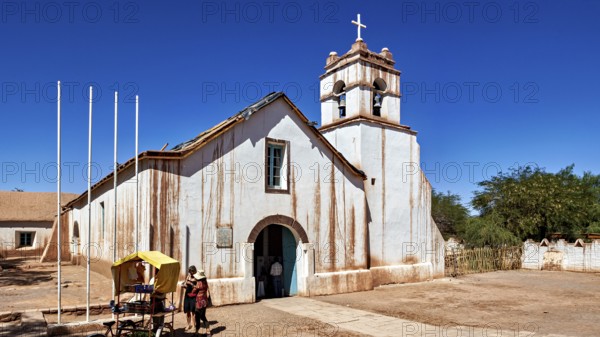 Church under a clear blue sky with people in the foreground and a cross on the tower, The church of San Pedro de Atacama in Chile