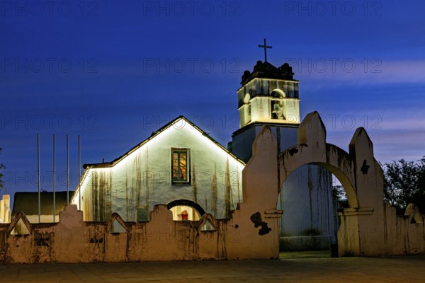 Church at dusk with illuminated tower and cross in front of a deep blue sky, The church of San Pedro de Atacama in Chile