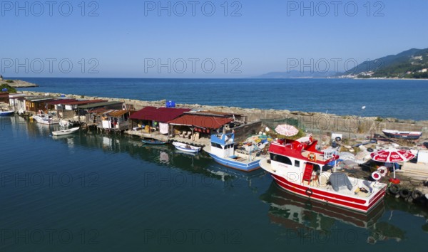Fishing harbour with colourful boats and huts along a quiet coastline under a clear sky, aerial view, Ginolu, Kastamonu province, Turkey