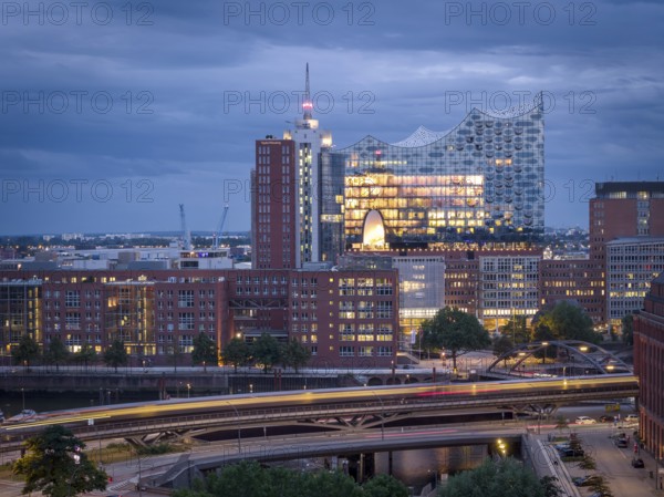 Evening city view with illuminated Elbphilharmonie, underground U3 and Speicherstadt under cloudy sky, Hamburg, Germany