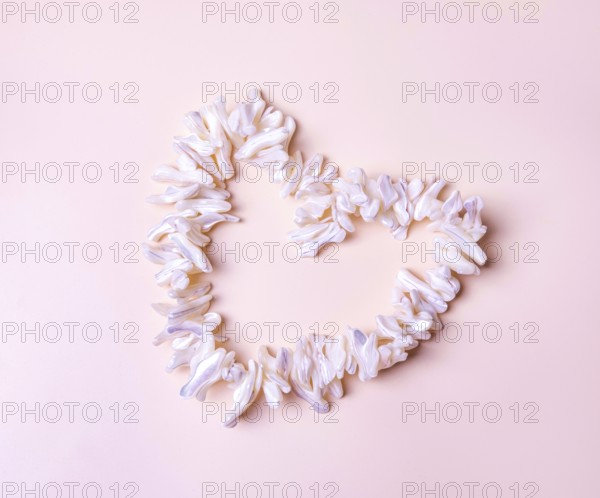 Heart made of mother-of-pearl white shells, on beige background, copy space