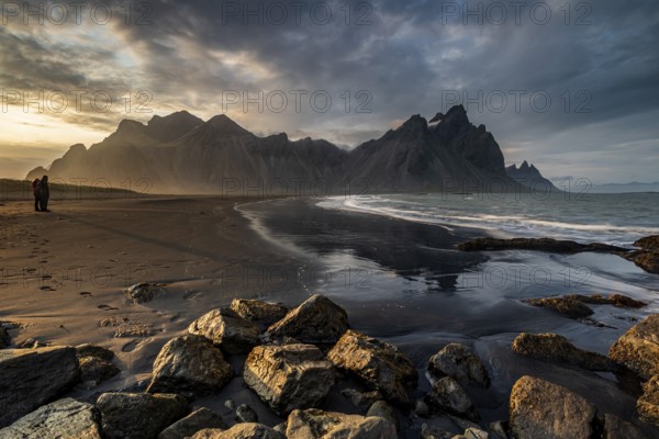 Two people standing on the beach, couple, adult, mountains, mountain range, sea, waves, surf, reflection, clouds, evening light, coast, summer, Vestrahorn, Stokksnes, Höfn, Iceland