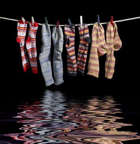 Clothesline with some multicolored sox fixed with clothes pins over reflective water surface in black back
