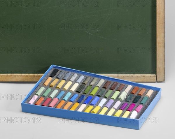 Edge of a old used blackboard and a box of crayons in front. Studio photography in light grey back