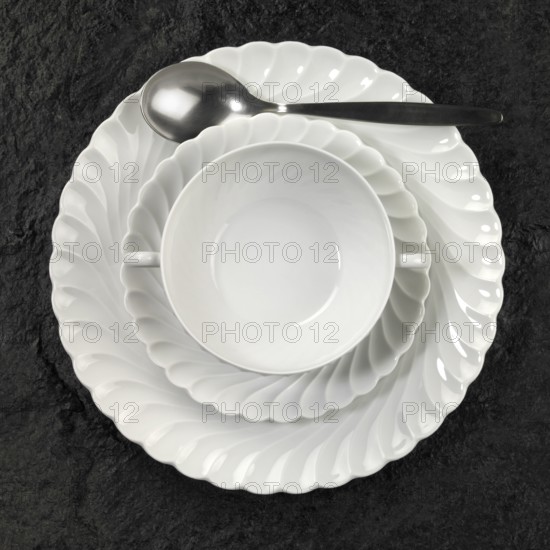 Studio photography of white porcelain plates and spoon on dark stone surface seen from above