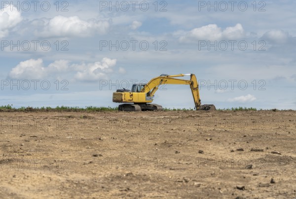 Yellow excavator at the horizon on earthen ground