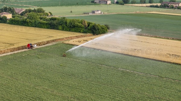 Modern agricultural irrigation technology applied to soybean crops utilizing a rain gun sprinkler system for efficient water distribution across fertile lands in springtime Italy's Po Valley