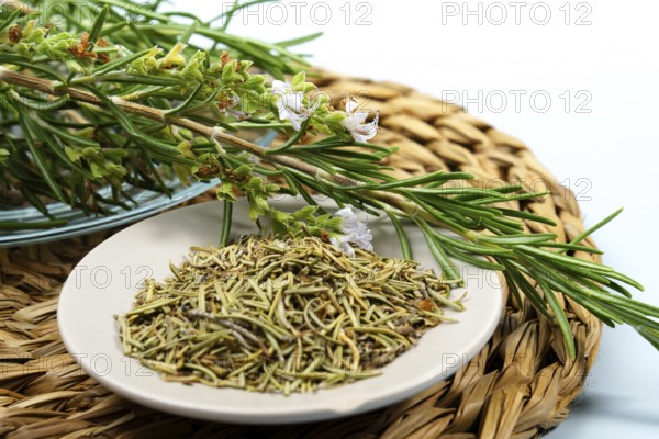Fresh rosemary sprigs with flowers lie on a plate of dried rosemary, ready for culinary or medicinal use