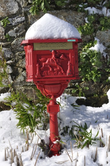 Vintage red mailbox under the snow, Ornate red mailbox covered in snow against a stone wall with green plants