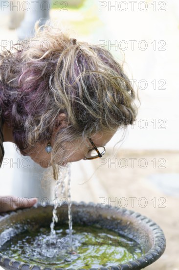 Woman refreshing herself by drinking water directly from a park fountain