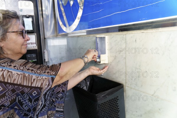 Woman disinfecting hands with antibacterial gel dispenser for coronavirus prevention