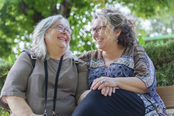 Two cheerful women enjoying each other's company on a park bench, representing lgbtq love, happiness, and togetherness