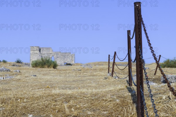 Rusty fence protecting an archeological site with ancient ruins under a clear blue sky, Malaga, Spain
