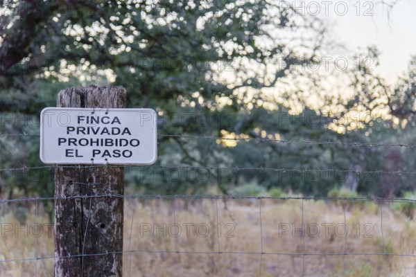 No trespassing sign in spanish (finca privada, prohibido el paso) attached to a barbed wire fence post