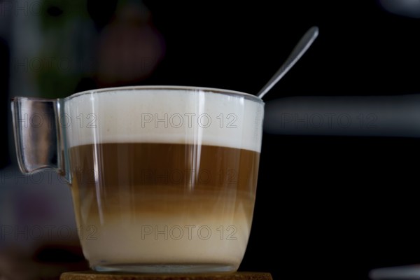 Latte macchiato in a glass cup with a spoon resting on the foam, showing the distinct layers of espresso, milk, and foam