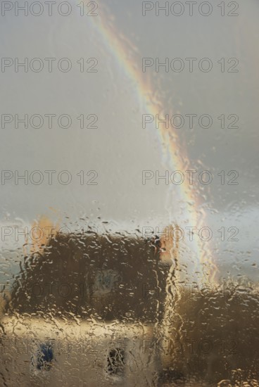 A house seen through a rain-soaked window with a rainbow arching across a gray sky, Old house seeing accross a window