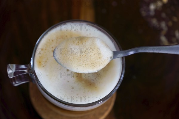 Creamy coffee foam being lifted by a spoon from a glass cup, creating a close-up view of the rich texture and frothy bubbles