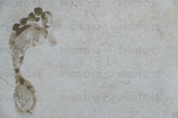 Muddy footprint marking a gray concrete surface with cracks, symbolizing evidence, trace, or passage