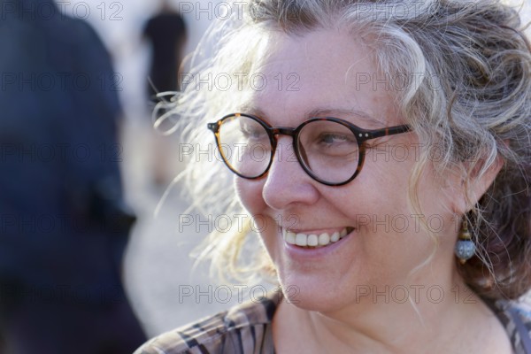 Close-up of cheerful mature woman with eyeglasses, enjoying golden hour sunlight, showcasing a genuine and happy expression