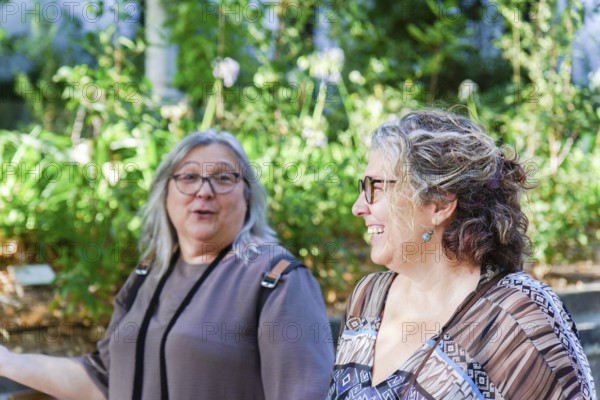 Two happy middle-aged women enjoying a conversation in a botanical garden, surrounded by lush greenery
