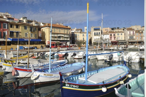 Cassis, the port, A vibrant harbor scene with colorful boats floating in calm water, lined by picturesque buildings under a clear blue sky