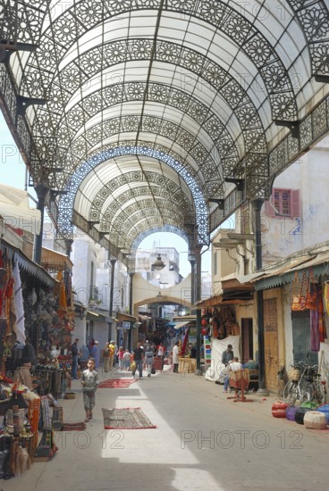 A vibrant market street with ornate metal canopy, bustling with people and colorful merchandise. Medina of Rabat in Marocco