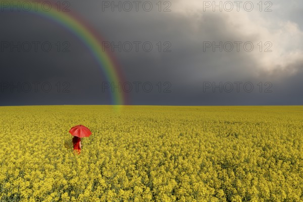 Woman with red umbrella in rape field rainbow