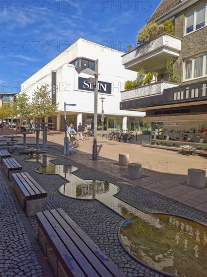 Pedestrian zone with fountain, department stores', pedestrians, traffic-calmed, young trees, residential building, balconies, old town, architecture, shops, people, blue sky, sunshine, Brühl, North Rhine-Westphalia, Germany